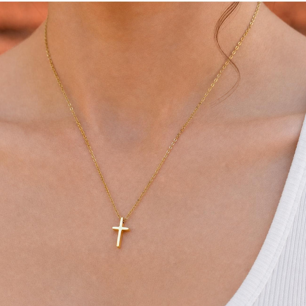 Gold plated necklace featuring a delicate chain and a small, simple cross pendant. The metal has a polished finish, and the cross is suspended centrally from the thin, linked chain, resting against the collarbone area.