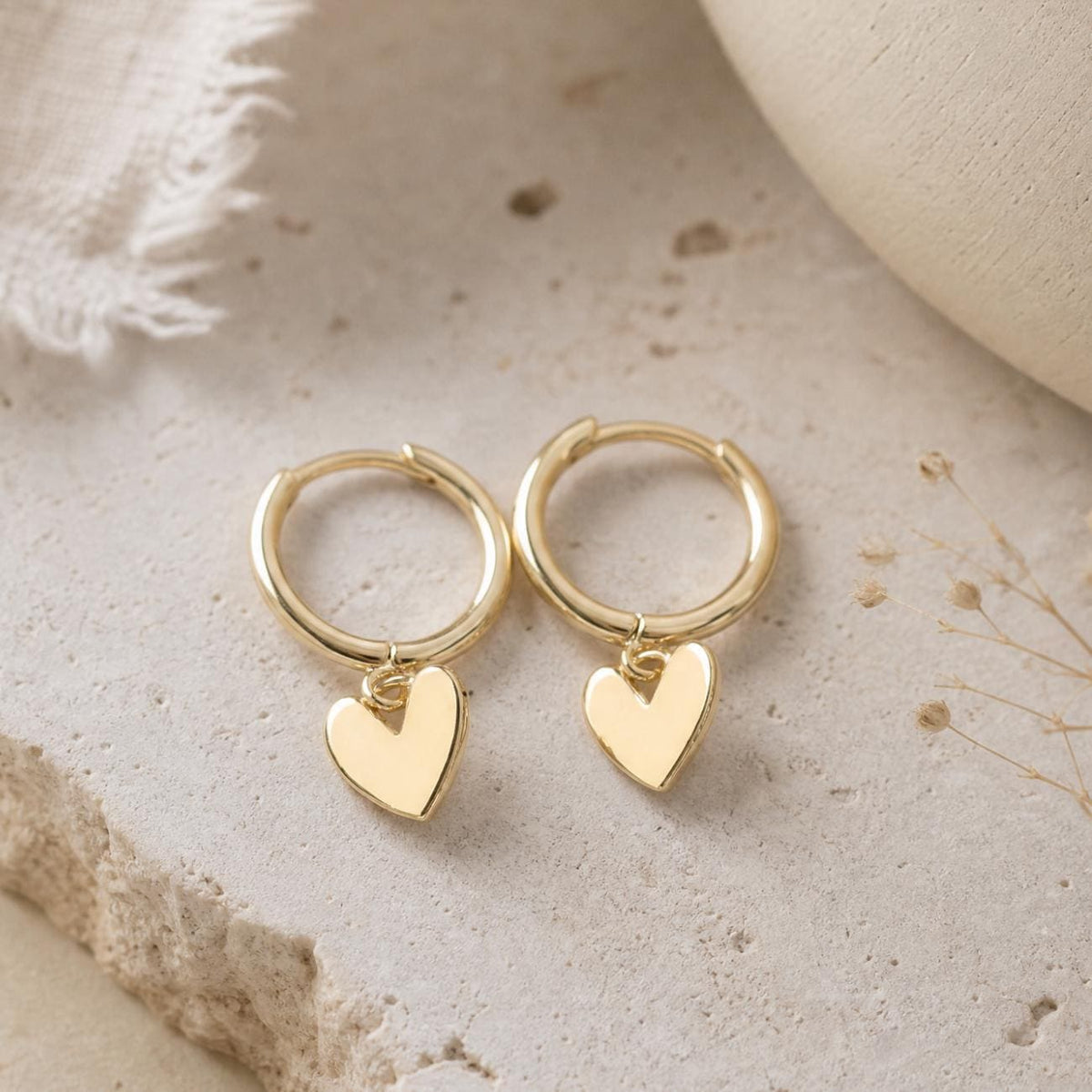 Gold heart huggie earrings, dainty style with dangle hearts, the earrings are styled on  a stone background
