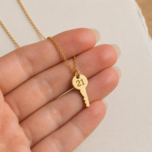 female hand holding a gold key necklace with the engraving 21 to celebrate a milestone 21st birthday