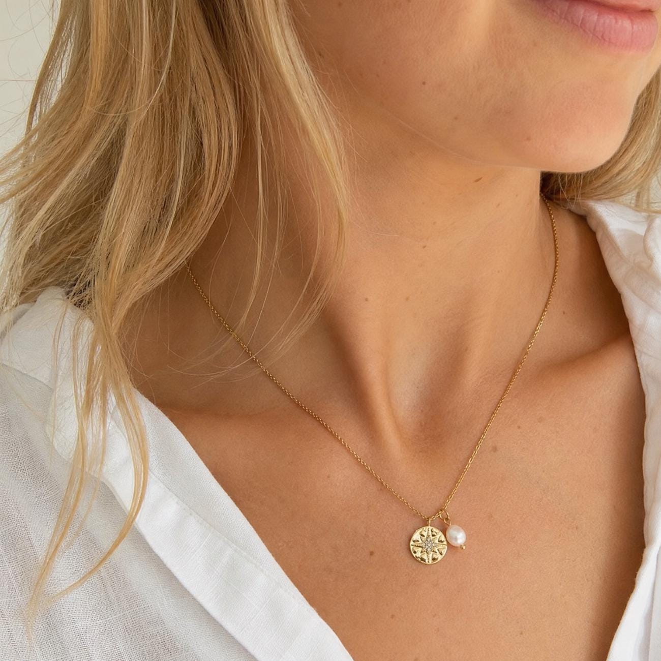 blonde female model wearing a guiding star pendant in gold with faux pearl charm both suspended on gold chain model wears white shirt