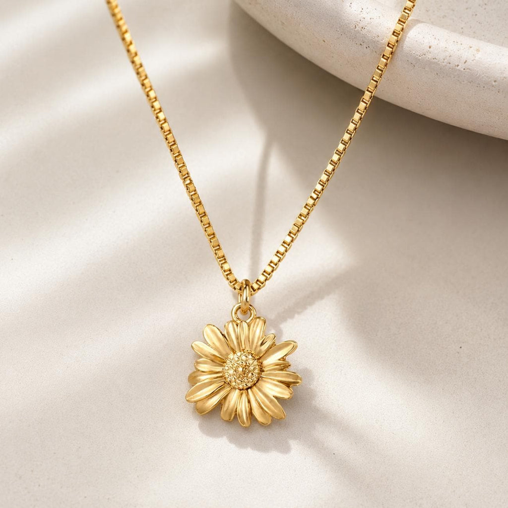 Gold plated sunflower necklace featuring a delicate box chain and a pendant shaped like a daisy flower. The flower pendant has textured, layered petals and a detailed, granular centre, all rendered in a consistent metallic gold finish.