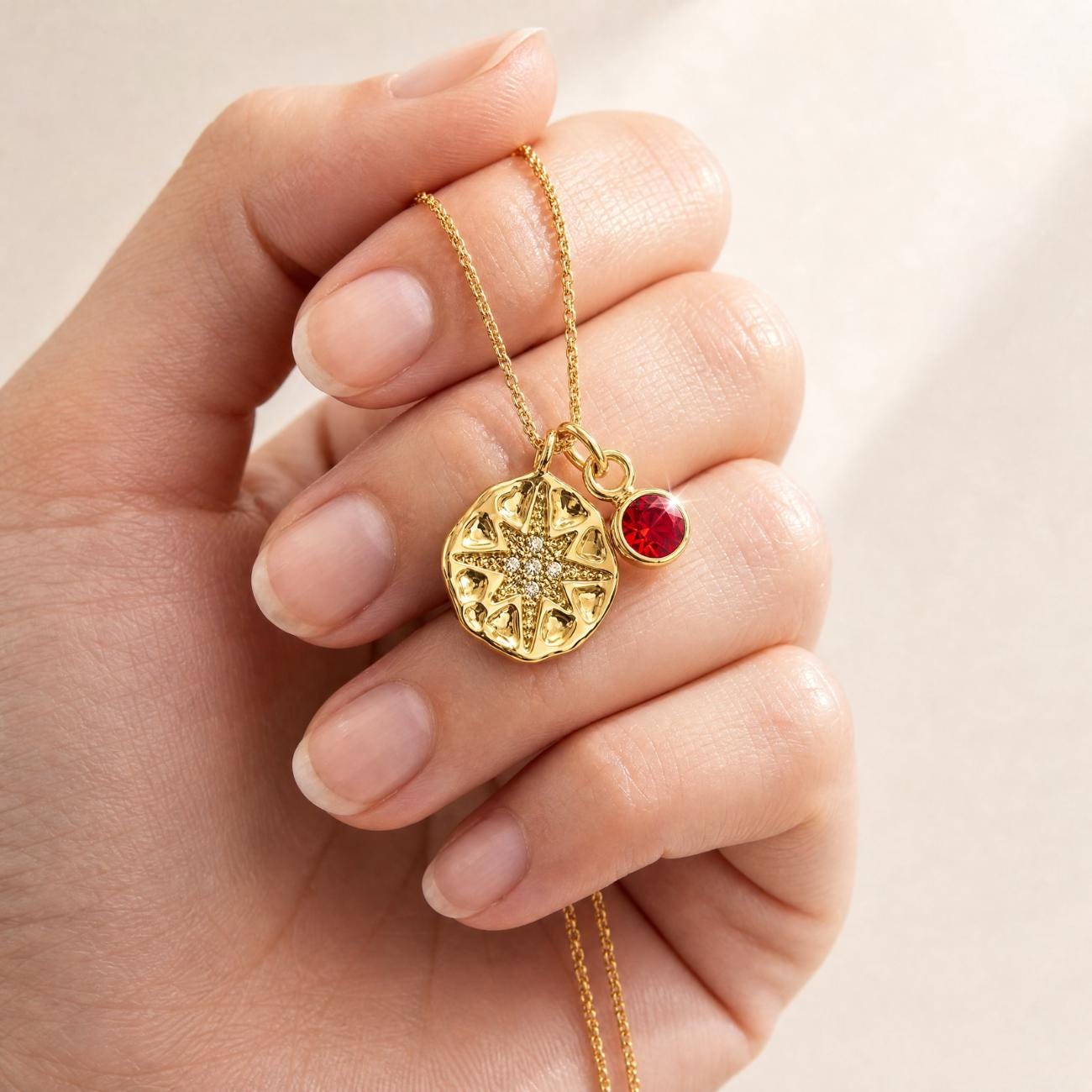 north star necklace in gold with birthstone charm both suspended on gold chain held by female model hand on neutral background
