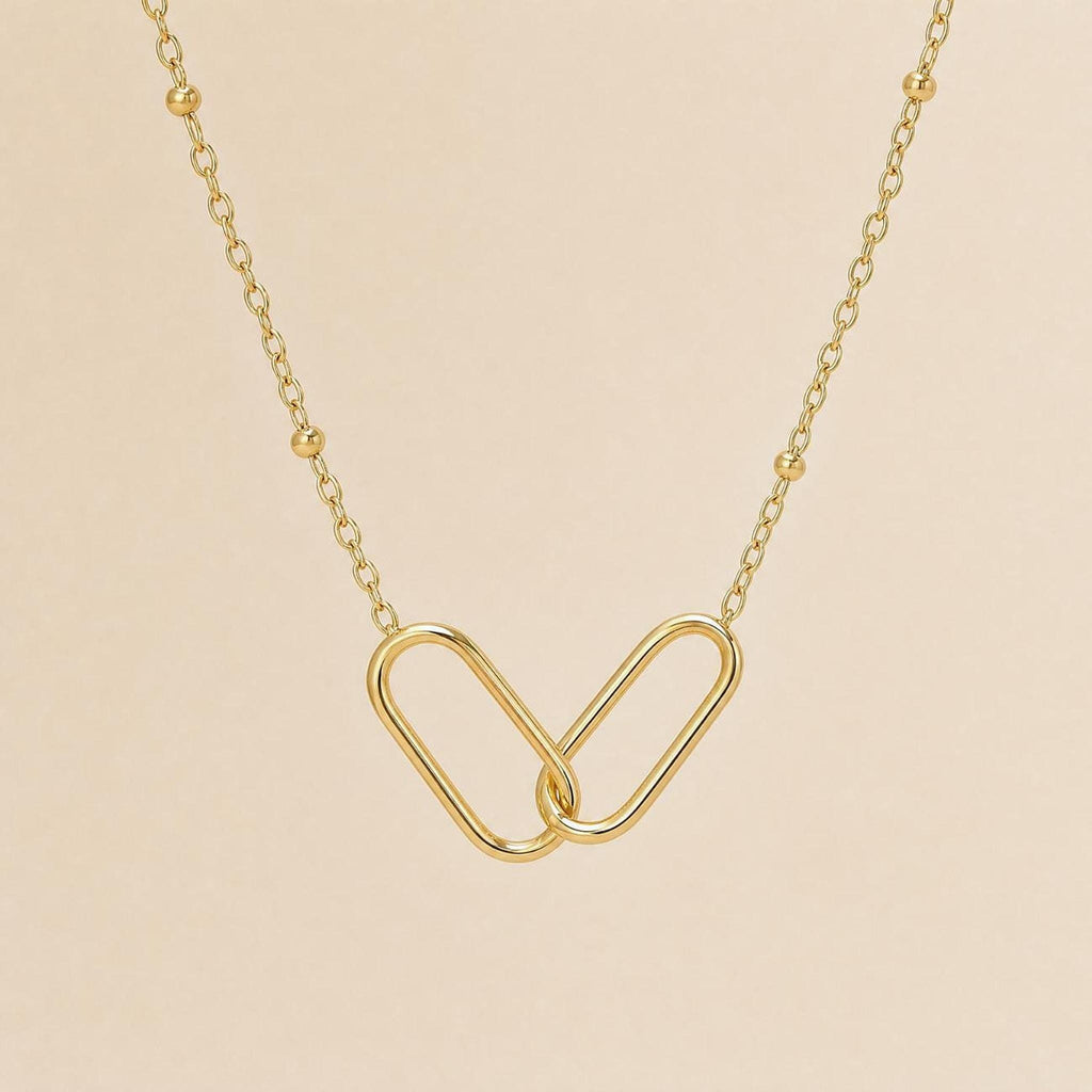 A close-up, overhead view of a gold interlocking link necklace with a beaded chain on a light beige background.