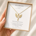 A gold phoenix necklace with a delicate chain and a cutout phoenix pendant, displayed in an open white gift box with text "ELOWEN LANE" and "NEW BEGINNINGS".