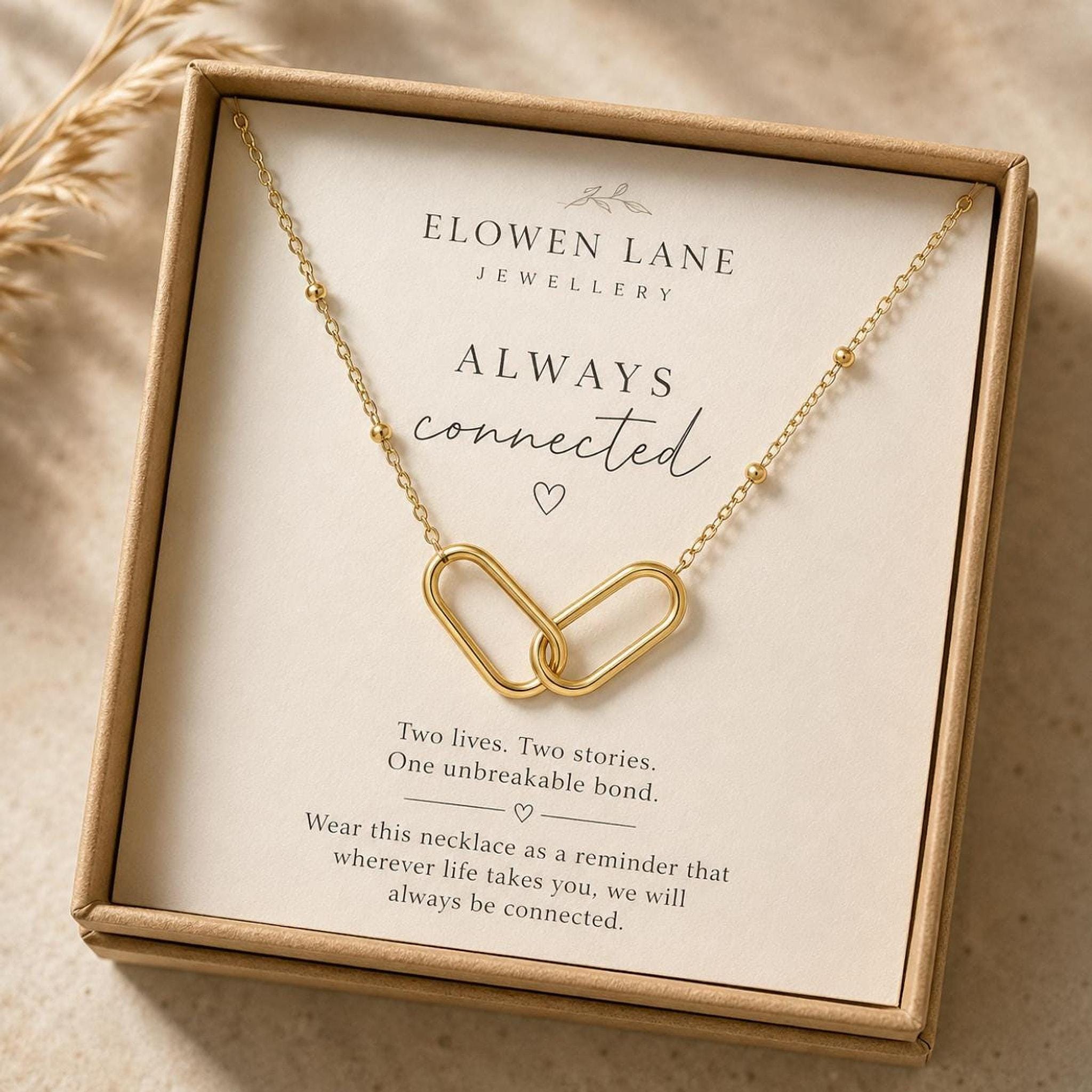 A gold interlocking link necklace with a beaded chain is displayed in an open brown gift box with text that reads "Always connected."