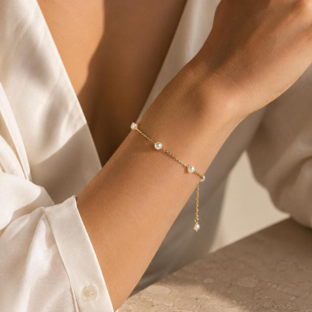 A thin gold chain bracelet with spaced small round white pearls worn on a person's wrist.