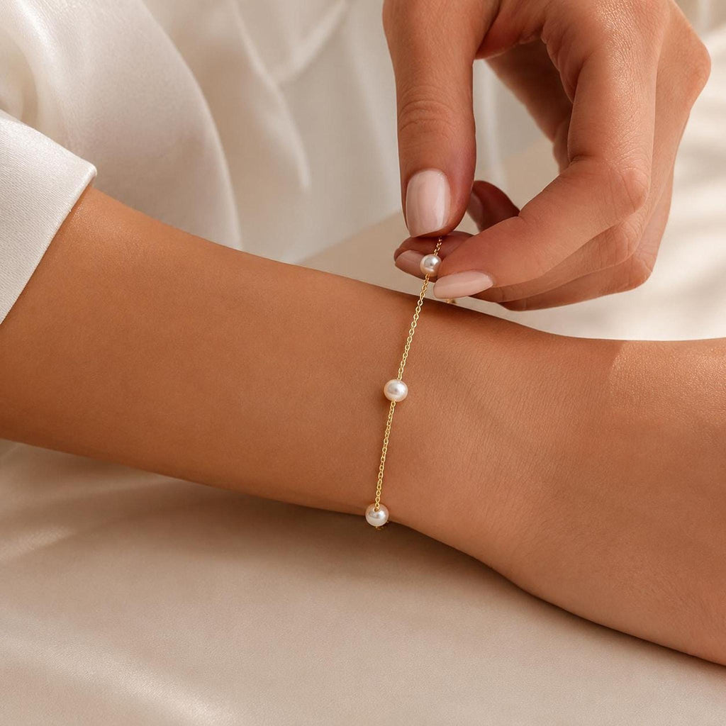 A hand adjusts a gold chain bracelet with scattered pearls resting on an arm.