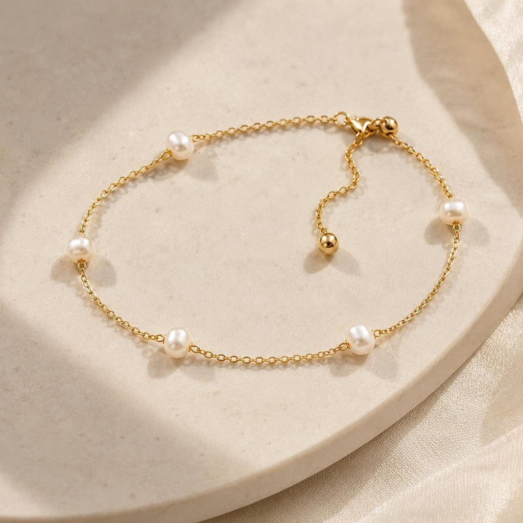 A delicate gold link bracelet featuring interspersed pearls and an adjustable sliding bead laid on a light surface.