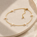 A delicate gold link bracelet featuring interspersed pearls and an adjustable sliding bead laid on a light surface.