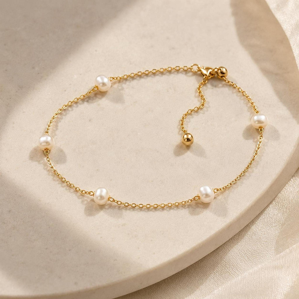 A delicate gold link bracelet featuring interspersed pearls and an adjustable sliding bead laid on a light surface.