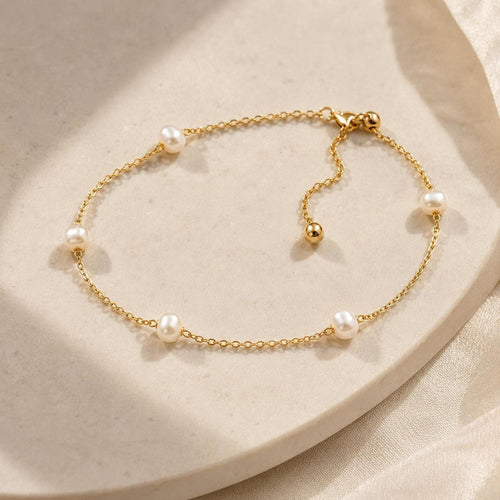 A delicate gold link bracelet featuring interspersed pearls and an adjustable sliding bead laid on a light surface.