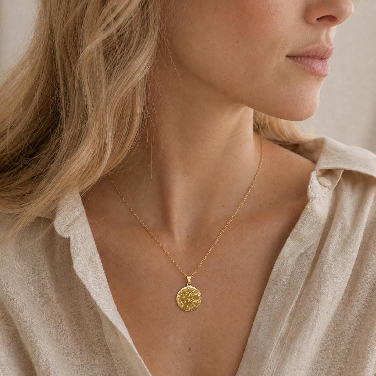 A gold plated necklace featuring a circular pendant with an engraved celestial design. The pendant displays a sun, a crescent moon, and small stars on its surface, suspended from a delicate, thin gold-toned metal chain.
